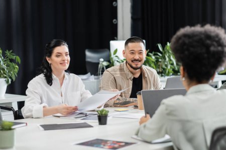 gente de negocios interracial alegre mirando a colega femenino mientras que trabaja en coworking moderno