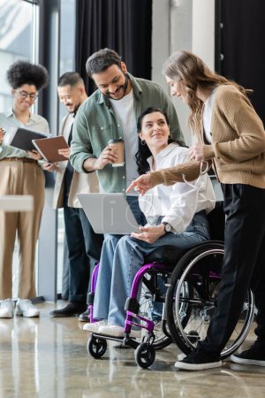 mujer discapacitada en silla de ruedas discutiendo proyecto de startup con feliz equipo interracial en coworking
