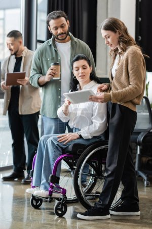 disabled woman in wheelchair looking at tablet, discussing startup project with interracial team