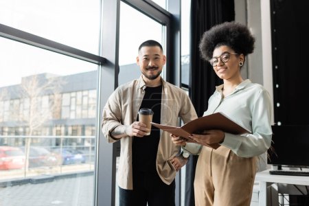asian businessman with coffee and african american woman looking at camera in office, coworking
