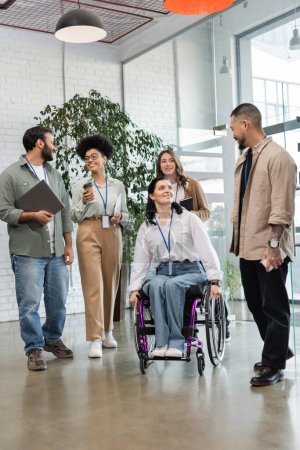 diversity and inclusion, disabled woman in wheelchair looking at asian colleague near team