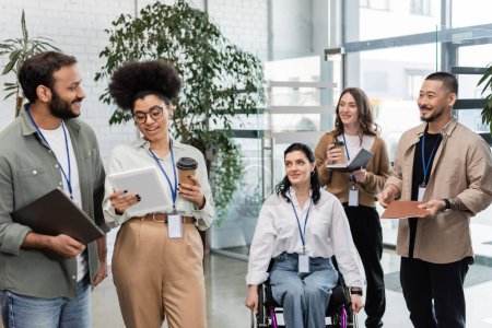 diversidad e inclusión, mujer discapacitada en silla de ruedas cerca de compañeros de trabajo interracial con etiquetas de nombre