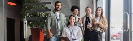 diverso equipo de startups mirando a la cámara y posando en la oficina, pancarta de gente de negocios interracial
