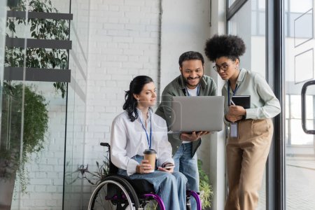group shot of diverse business people, disabled woman on wheelchair looking at laptop with coworkers