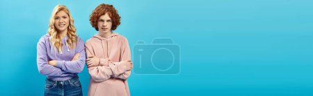 Photo for Displeased teenage friends in hoodies looking at camera with crossed arms on blue, banner - Royalty Free Image