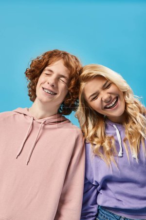 amigos adolescentes llenos de alegría en sudaderas con capucha con estilo riendo con los ojos cerrados en azul, adolescentes despreocupados