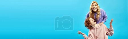 Photo for Laughing blonde teen girl having fun near discouraged redhead boyfriend on blue, banner - Royalty Free Image