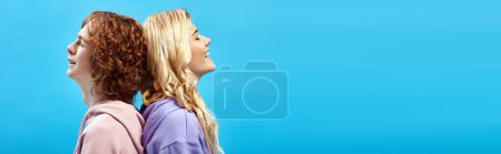Photo for Happy teenage friends sitting back to back and smiling with closed eyes on blue, side view, banner - Royalty Free Image