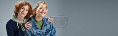 rousse adolescent gars câlin épaules de heureux blonde copine sur gris, jeune mode, bannière