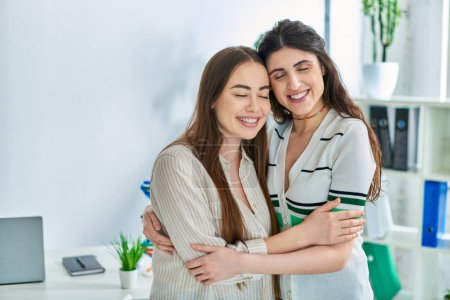 Foto de Alegre pareja lesbiana sonriendo con los ojos cerrados y abrazándose calurosamente, concepto de fertilización in vitro - Imagen libre de derechos