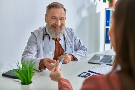 fröhlicher Arzt lächelt aufrichtig seine brünette Patientin an und zeigt ihm einen Schwangerschaftstest, ivf concept