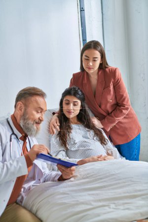 smiley grey bearded doctor showing ultrasound of their baby to focused lgbt couple, ivf concept