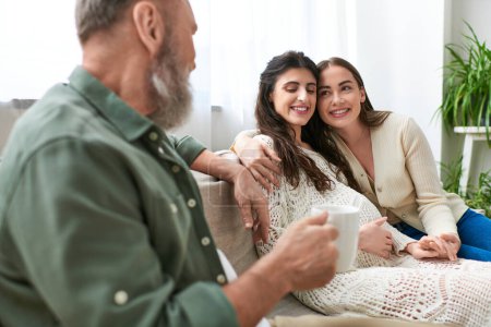 happy lgbt couple sitting on sofa and hugging, grey bearded man looking at his daughter, ivf concept