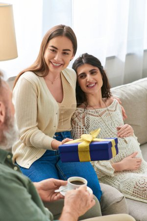 happy pregnant woman hugging with her partner with gift in hands looking at her father, ivf concept
