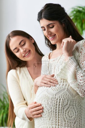 beautiful lgbt couple hugging and smiling cheerfully with hands on pregnant belly, ivf concept