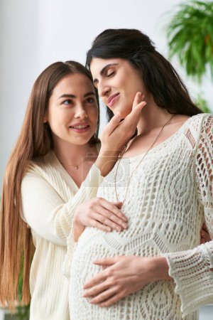 happy lgbt couple smiling cheerfully with hands on pregnant belly, hand to chin, ivf concept