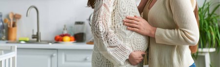 pretty lesbian couple hugging touching pregnant belly with kitchen on backdrop, ivf concept, banner