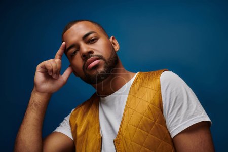 handsome man in trendy yellow vest with finger next to face and stylish earring, fashion concept