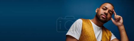 handsome african american man with beard and earring in trendy yellow vest, fashion concept, banner