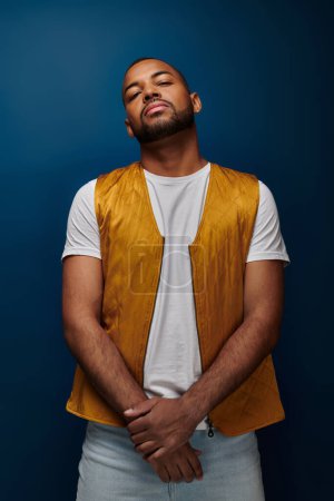 handsome african american man in vest posing standing still on dark blue background, fashion concept