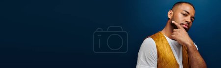 Photo for Young man in stylish yellow vest posing on dark blue backdrop, hand to face, fashion concept, banner - Royalty Free Image