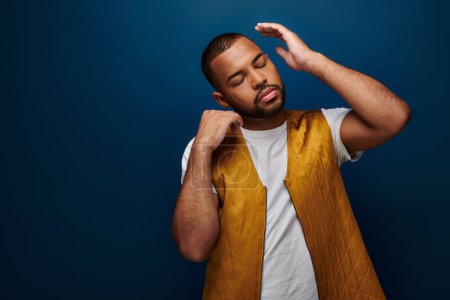 stylish young man in trendy yellow vest posing with closed eyes and hands near face, fashion concept