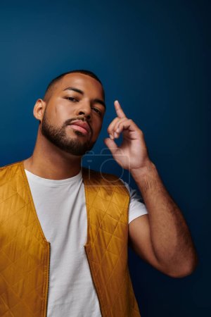 homme afro-américain à la mode avec la barbe regardant la caméra et pointant son doigt vers le haut, concept de mode