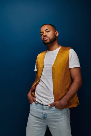african american man posing on dark blue backdrop with hands in jeans pockets, fashion concept