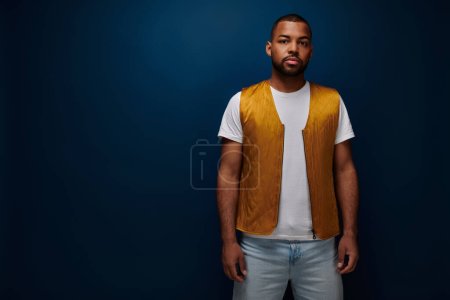 Photo for Handsome bearded man in yellow trendy vest standing still on dark blue backdrop, fashion concept - Royalty Free Image