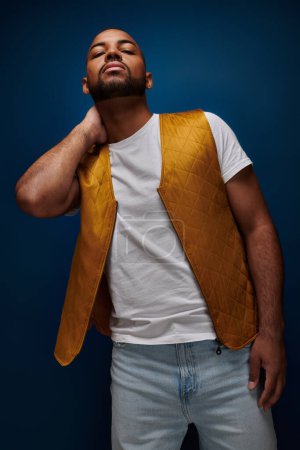 Foto de Hombre afroamericano guapo en chaleco amarillo posando con su mano detrás de su cuello, concepto de moda - Imagen libre de derechos