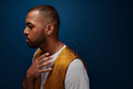 young handsome man with diamond earring posing in profile on dark blue backdrop, fashion concept