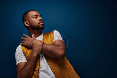 Photo for Young bearded man in yellow vest slightly bending over to back with hands on chest, fashion - Royalty Free Image