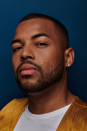trendy african american male model with beard and diamond earring looking at camera, fashion concept