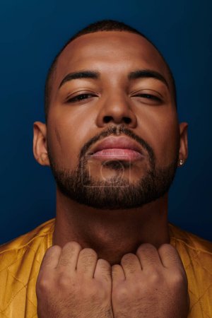homme afro-américain avec boucle d'oreille et barbe regardant caméra avec les mains sur le col, concept de mode