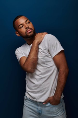 junger Afroamerikaner in weißem Hemd und Jeans gestikulierend und wegschauend, Modekonzept