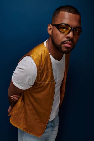 stylischer afrikanisch-amerikanischer Mann in gelber Weste und Sonnenbrille blickt in die Kamera, Modekonzept
