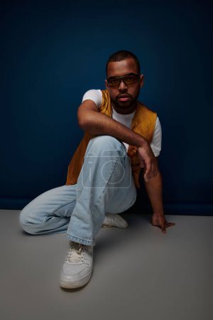 handsome african american man with sunglasses and earring posing on floor, fashion concept