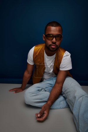 handsome man in yellow vest and sunglasses sitting on floor looking at camera, fashion concept