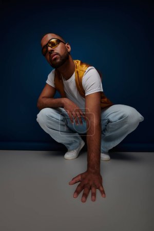Photo for Stylish african american man squatting and looking at camera, hand on floor, fashion concept - Royalty Free Image