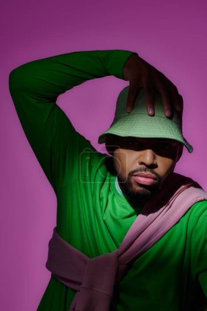 Téléchargez les photos : Beau modèle masculin afro-américain posant avec sa main sur panama vert, concept de mode - en image libre de droit