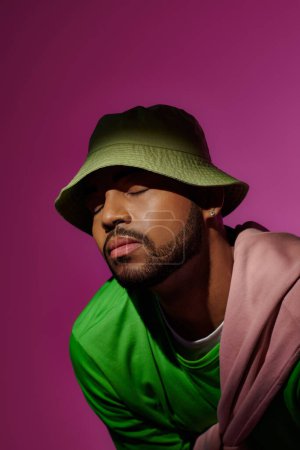 bärtiger afrikanisch-amerikanischer Mann in grünem Panama mit geschlossenen Augen vor violettem Hintergrund, Modekonzept
