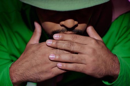 Téléchargez les photos : Gros plan de l'homme afro-américain en panama vert avec les mains sous le menton sur fond violet, la mode - en image libre de droit