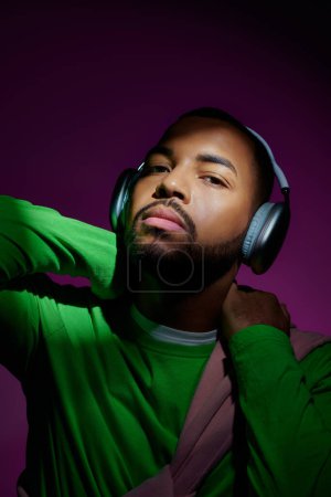 hombre afroamericano guapo con barba en auriculares sobre fondo púrpura, concepto de moda