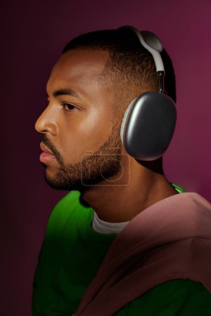 junge stilvolle männliche Modell posiert im Profil mit Kopfhörern auf lila Hintergrund, Modekonzept