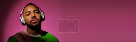 Téléchargez les photos : Jeune modèle masculin afro-américain avec écouteurs sur fond rose, concept de mode, bannière - en image libre de droit