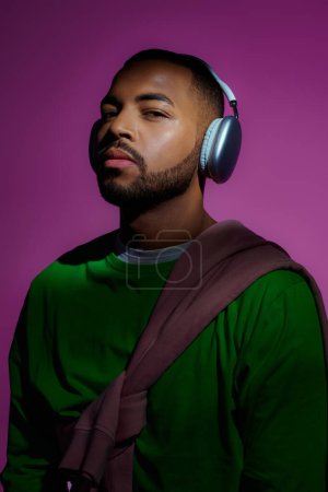 beau modèle masculin afro-américain en sweat-shirt vert avec écouteurs, concept de mode