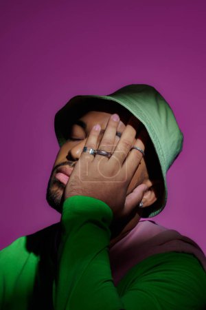 Foto de Guapo hombre con estilo en panama verde con accesorios poniendo su mano en la cara, concepto de moda - Imagen libre de derechos
