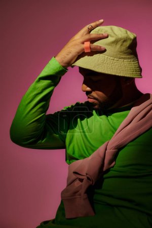 schöner bärtiger Mann mit Ringen posiert im Profil mit der Hand auf grünem Panama, Modekonzept