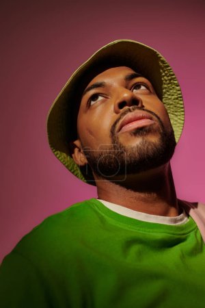 Photo for Good looking bearded man in green panama and sweatshirt looking away on pink backdrop, fashion - Royalty Free Image