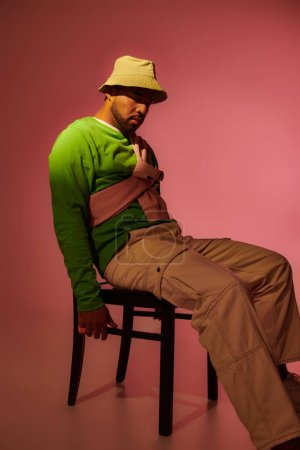 good looking african american man in green sweatshirt and panama sitting on chair, fashion concept